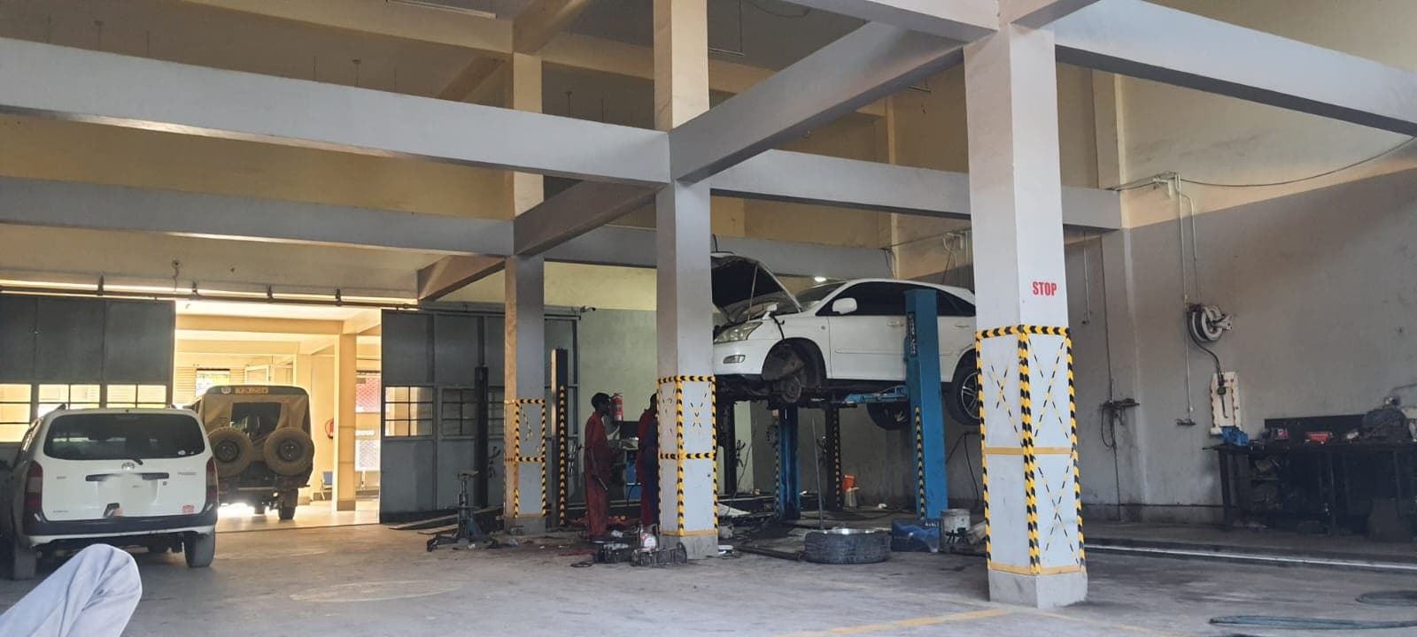 Sedan raised on a two-post lift with mechanics servicing it in the workshop bay